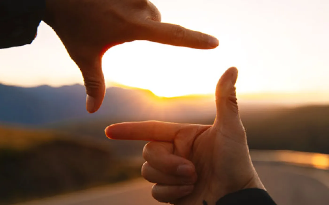 Hands framing a sunset over a winding road, symbolizing the importance of looking at the bigger picture when planning for retirement.