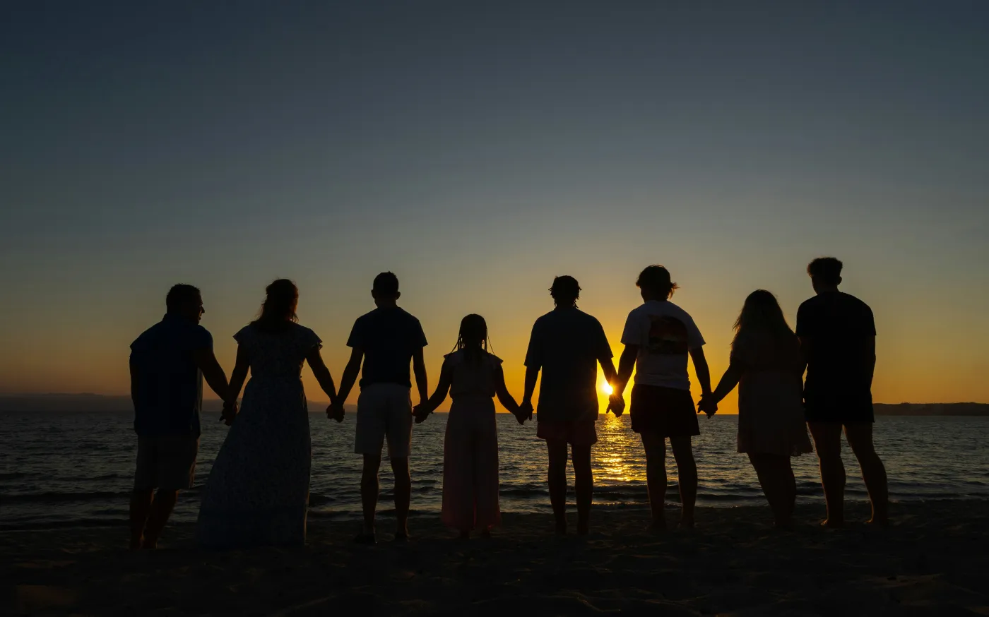 Family holding hands while walking on the beach at sunset representing retirement, legacy, and financial security