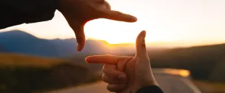 Hands framing a sunset over a winding road, symbolizing the importance of looking at the bigger picture when planning for retirement.