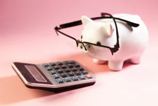 Piggy bank with glasses looking at a calculator, representing retirement planning and budgeting