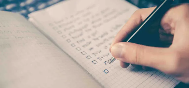 Person writing a list of financial goals in a notebook to plan for retirement and life priorities. 