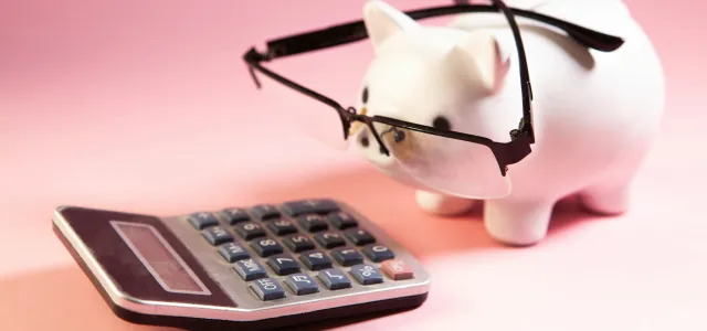 Piggy bank with glasses looking at a calculator, representing retirement planning and budgeting
