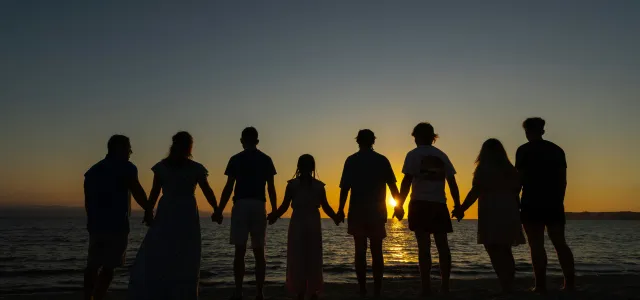 Family holding hands while walking on the beach at sunset representing retirement, legacy, and financial security